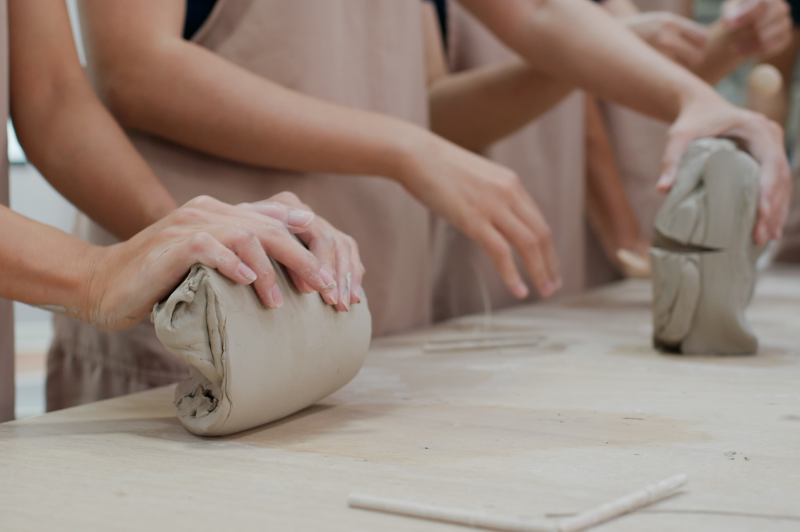 Shot of people's hands moulding clay on a bench.